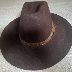 Dark brown cowboy hat with lighter brown braided leather trim with feathers.